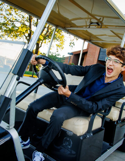 Bar Mitzvah boy laughing and pretending to drive a golf cart during golden hour at Union League Liberty Hill, captured by PCSI – fun, candid, and natural event photography