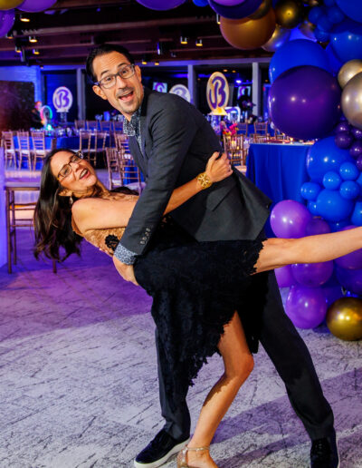 Candid Bar Mitzvah photography of parents sharing a playful dance in front of the event décor at Union League Liberty Hill, photographed by PCSI – elegant and candid Mitzvah photography.