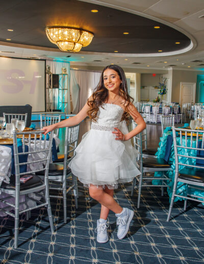 Bat mitzvah girl posing in a white dress surrounded by elegant peacock feather-inspired blue and purple decor at Philmont Country Club in Philadelphia, photographed by PCSI PHOTO