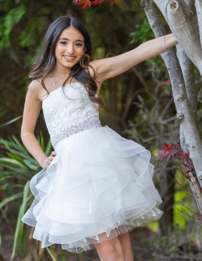 Bat Mitzvah girl poses gracefully beside a tree in her white ruffle dress celebrating at Philmont Country Club in Huntingdon Valley, Pennsylvania.