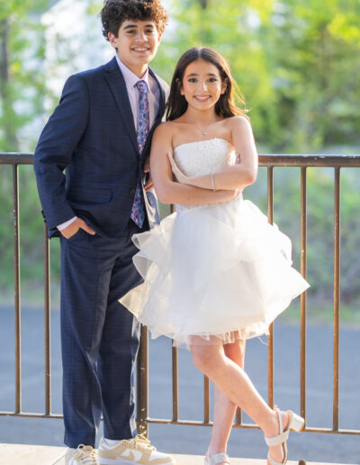 Bat Mitzvah girl in a white ruffle dress poses with her brother in a navy suit at Philmont Country Club during her celebration at the Philmont Country Club in Huntingdon Valley, Pennsylvania