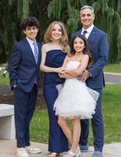 Bat Mitzvah girl in white ruffle dress stands with her parents and brother dressed in coordinated blue and lavendar attire before the celebration at Philmont Country Club in Huntingdon Valley, Pennsylvania.
