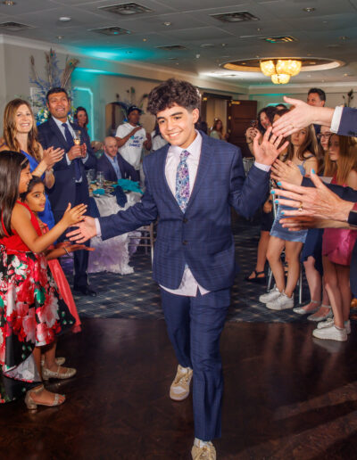 Bat Mitzvah girl's brother in a navy pin stripe suit walks through a cheering crowd, high-fiving guests during the celebration at Philmont Country Club in Huntingdon Valley, Pennsylvania.
