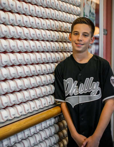Bar Mitzvah boy smiling in his black custom Philly baseball jersey in front of an elaborate wall of baseballs at Citizens Bank Park