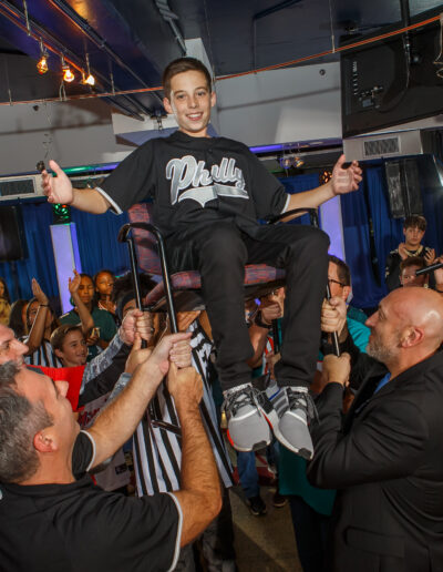 The Bar Mitzvah Boy Smiling as he is lifted high above the dance floor by friends and family at Citizens Bank Park