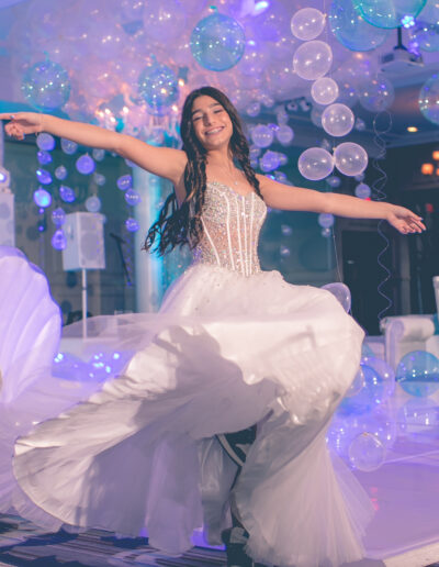 Bat Mitzvah girl twirling in her white beaded gown with high top Nike's lit by pink, purple and blue lighting and balloons on the dance floor at Vie by Cescaphe in Philly