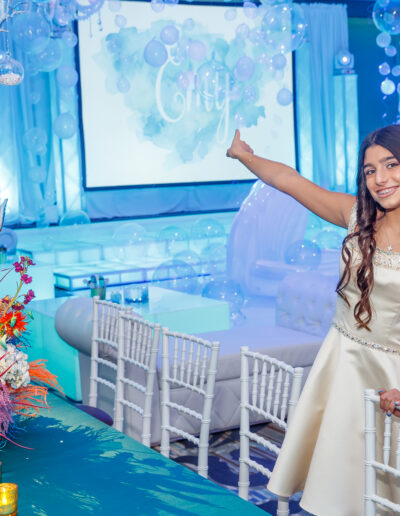 Cheerful Bat Mitzvah girl pointing to her custom and personalized dance floor surrounded by opal colored balloons and vibrant floral centerpieces at Vie by Cescaphe in Philly