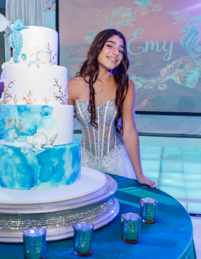 Bat mitzvah girl smiling confidently beside her ocean themed cake sitting on a jeweled cake stand on a turquoise illuminated custom dance floor at Vie by Cescaphe in Philadelphia