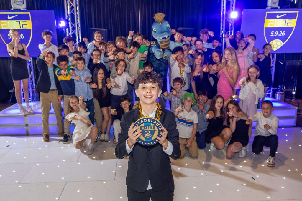 bar mitzvah child posing with friend group at lucky strike while holding a philadelphia union soccer team necklace chain