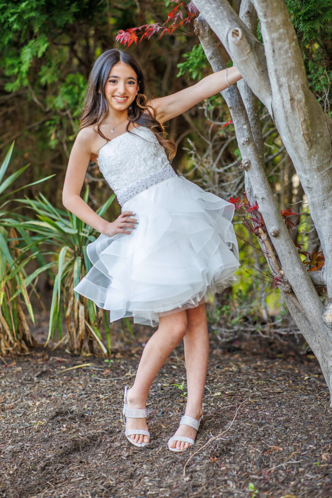 bat mitzvah girl wearing a white dress and posing next to a tree at shir ami synagogue in newtown pennslyvania